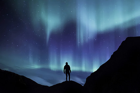 photo of person standing on mountain tops with a view of Aurora in the sky thumbnail