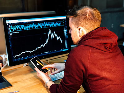 man holding smartphone sitting infront of computer monitor thumbnail