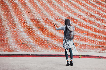 girl wearing backpack standing near orange brick wall thumbnail