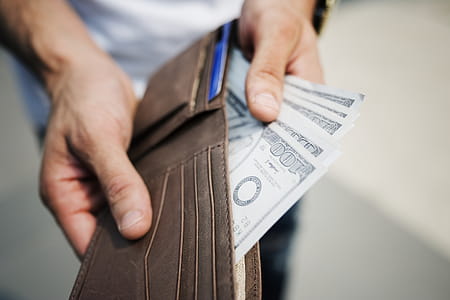 Man Holding Brown Leather Bi-fold Wallet With Money in It thumbnail