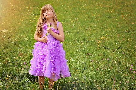 girl standing on grass field while holding flower thumbnail
