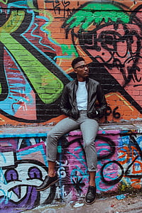 man with hands in pocket sitting beside wall thumbnail