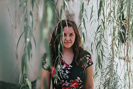 woman in black floral shirt standing near green leaves thumbnail