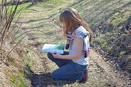 girl wearing white and brown stripe shirt and blue denim jeans reading a book while sitting in the ground during daytime thumbnail