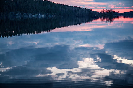 reflection of clouds on calm body of water near trees thumbnail