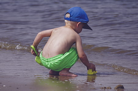 Boy In Blue Cap And Green Shorts Playing On Seashore thumbnail