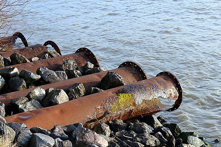 several brown metal pipes in front of body of water thumbnail