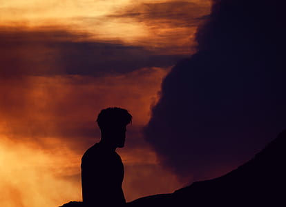 silhouette of a person standing under cloudy sunset sky thumbnail