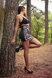 woman wearing spaghetti strap crop top and mini skirt leaning on tree trunk thumbnail