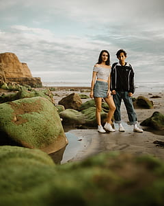 man and woman standing on seashore during cloudy skies thumbnail