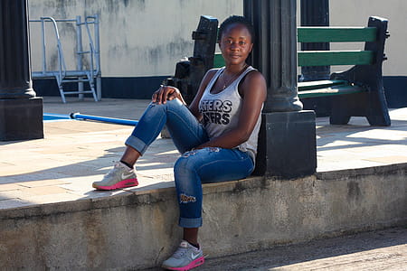 Woman Wearing White Tank Top Leaning on Post Sitting on Concrete Pavement thumbnail