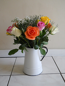orange, red, and pink rose flowers in white and black pitcher near the beige wall thumbnail