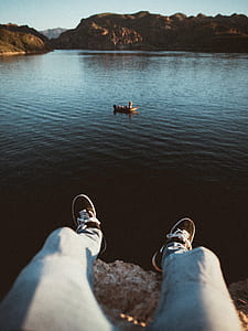 person sitting on cliff near body of water thumbnail
