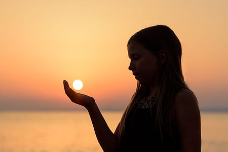 girl acting like the sun on her hands while near seashore during sunset thumbnail