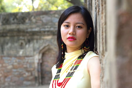 woman wearing yellow shirt leaning on brown concrete wall during daytime thumbnail