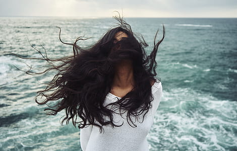 woman standing near sea with face covered with hair thumbnail