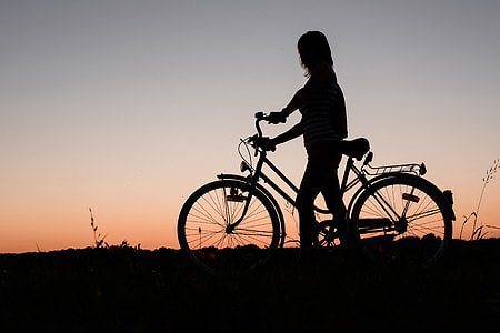 A silhouette of a woman with a bicycle at sunset thumbnail