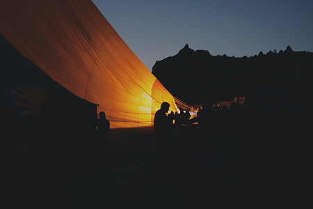 silhouette of people standing beside lighted hot air balloon thumbnail