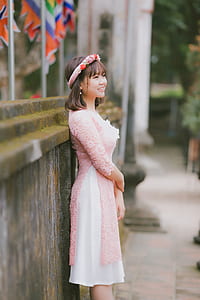 woman wearing pink floral long-sleeved dress leaning on concrete wall thumbnail