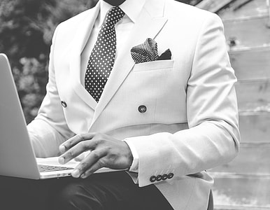 grayscale photo of man wearing white suit with laptop on lap thumbnail