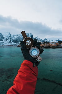 person holding up brass-colored compass at eye level outside with mountain range in background during twilight thumbnail