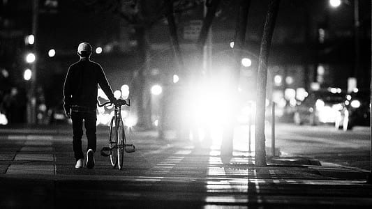 man walking beside his bike in grayscale photography thumbnail