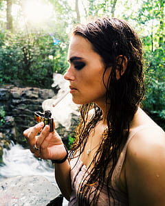 woman lighting a cigarette surrounded by trees thumbnail