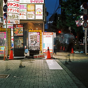 time-lapse photography of person crossing street near lighted building at night time thumbnail