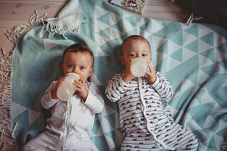 two toddler laying on teal textile while drinking feeding bottles thumbnail