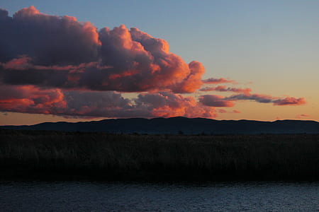 silhouette photo of mountain with clouds near body of water thumbnail