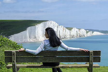 woman in white sweatshirt sitting on wooden bench near cliff during daytime thumbnail