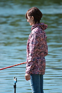 Selective Focus Photography of Woman Holding Red Fishing Rod Standing Beside Calm Body of Water thumbnail