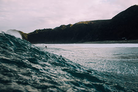photo of sea waves and silhouette of mountain under gray sky thumbnail