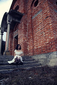 photo of woman wearing off-shoulder dress sitting on stair of brown concrete building thumbnail