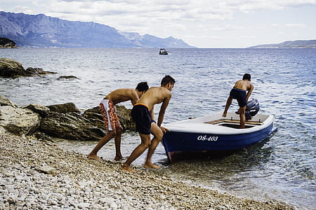 Three Men Pushing Speed Boat on Seashore thumbnail