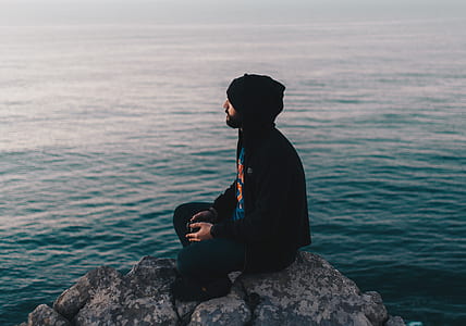 man in black hoodie jacket sitting on boulder surrounded by water thumbnail