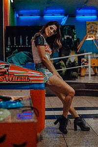 woman in blue denim shorts standing leaning on arcade machine thumbnail