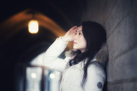 woman in white parka jacket standing beside gray wall thumbnail