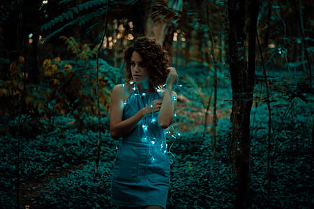 woman wearing blue sleeveless dress surrounded by green grass with string lights thumbnail