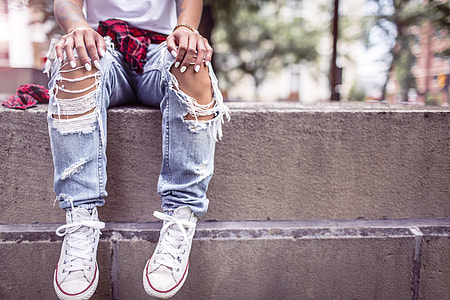 person in blue distressed jeans sitting on concrete wall thumbnail