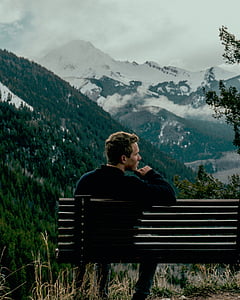 man sitting on bench in front of mountain during daytime thumbnail