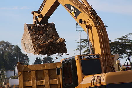 yellow Caterpillar excavator bucket filled with soil above yellow dump truck at daytime thumbnail