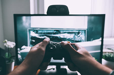 person holding game controller while playing in front turned on flat screen TV inside entertainment room thumbnail