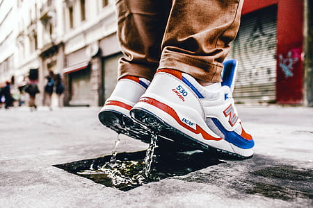 person standing on gray concrete top road wearing pair of white-blue-and-red New Balance lace-up low-top sneakers thumbnail