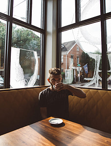 man in grey T-shirt sipping on white ceramic cup sitting on yellow leather sofa near window during daytime thumbnail