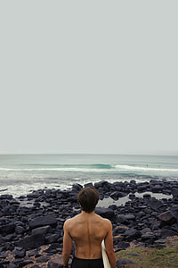 man carrying surfboard standing near shore thumbnail