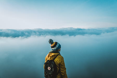 person wearing yellow jacket and bubble knit cap standing near white clouds at daytime thumbnail