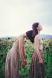 Two Woman Standing Near Sunflower Field at Cloudy Sky thumbnail