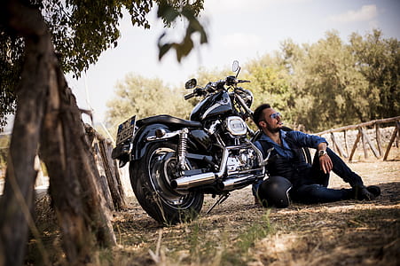 man sitting on grass near black cruiser motorcycle thumbnail