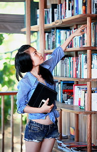 woman with blue sport shirt reaching of a book on a bookcase thumbnail